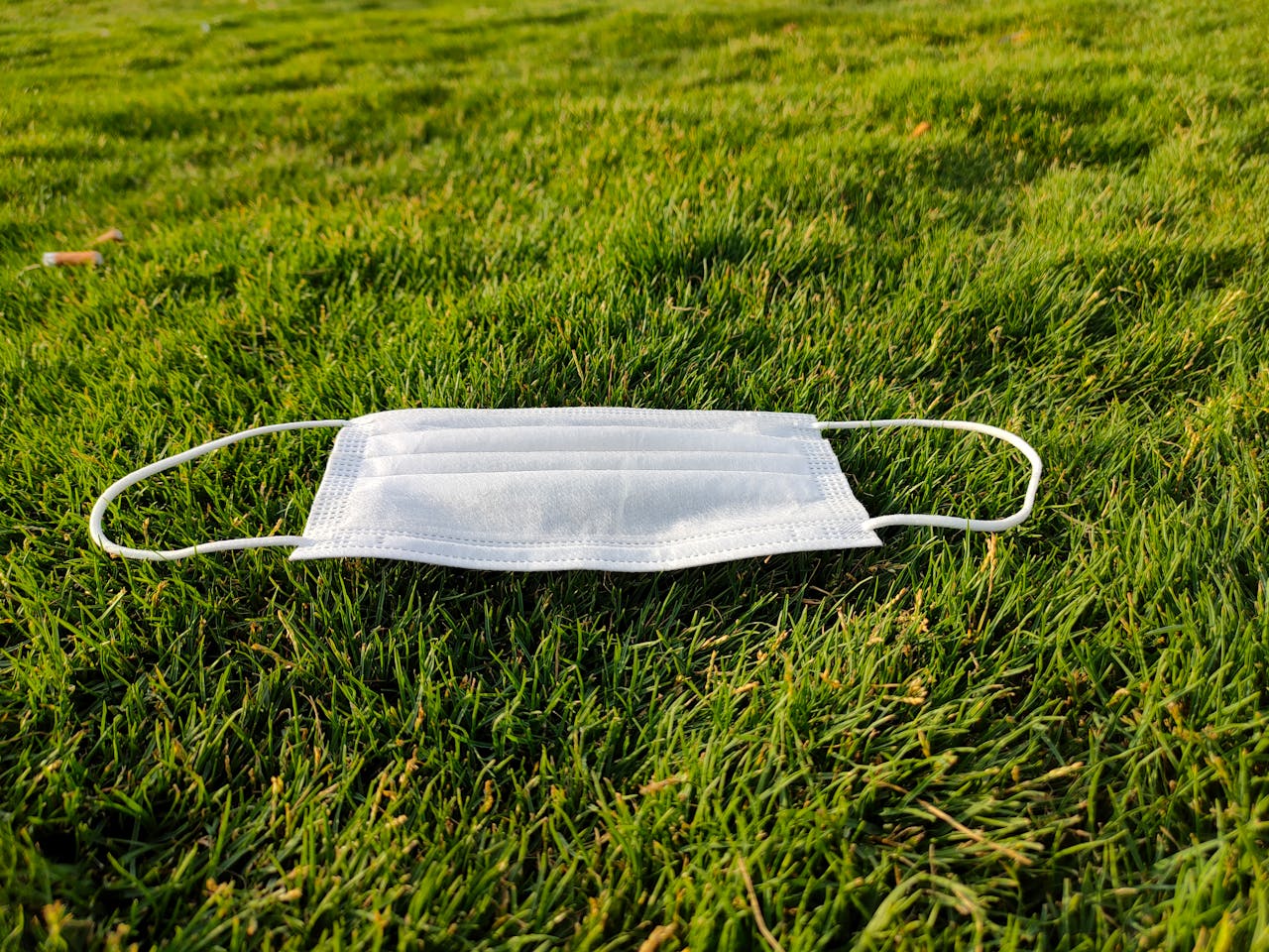 A close-up of a face mask lying on vibrant green grass, symbolizing post-pandemic pollution in Riyadh.